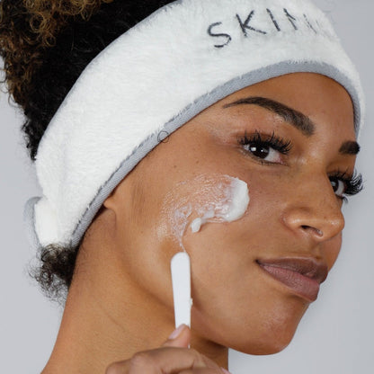 Image of a lady applying cleansing balm to her cheek, including a spatula.